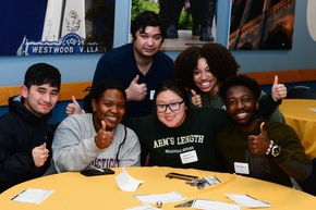 Smilling Gradaute students seating together, all giving thumbs up